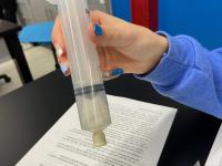 student holding a syringe, reaction inside producing gas.