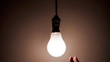 hand reaching from a hanging lit light bulb