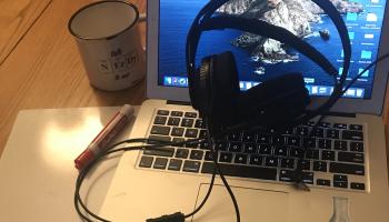 Image of a laptop with a headset on it with a small whiteboard and red marker, and a mug that says Talk Nerdy to Me 