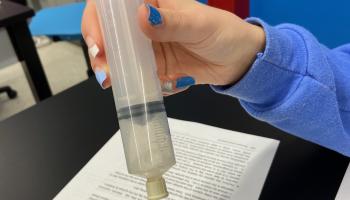 student holding a syringe, reaction inside producing gas.