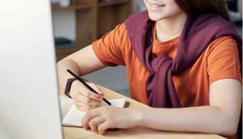 student in orange shirt looking at laptop screen
