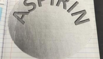 round shape with capital letters spelling ASPIRIN within a notebook