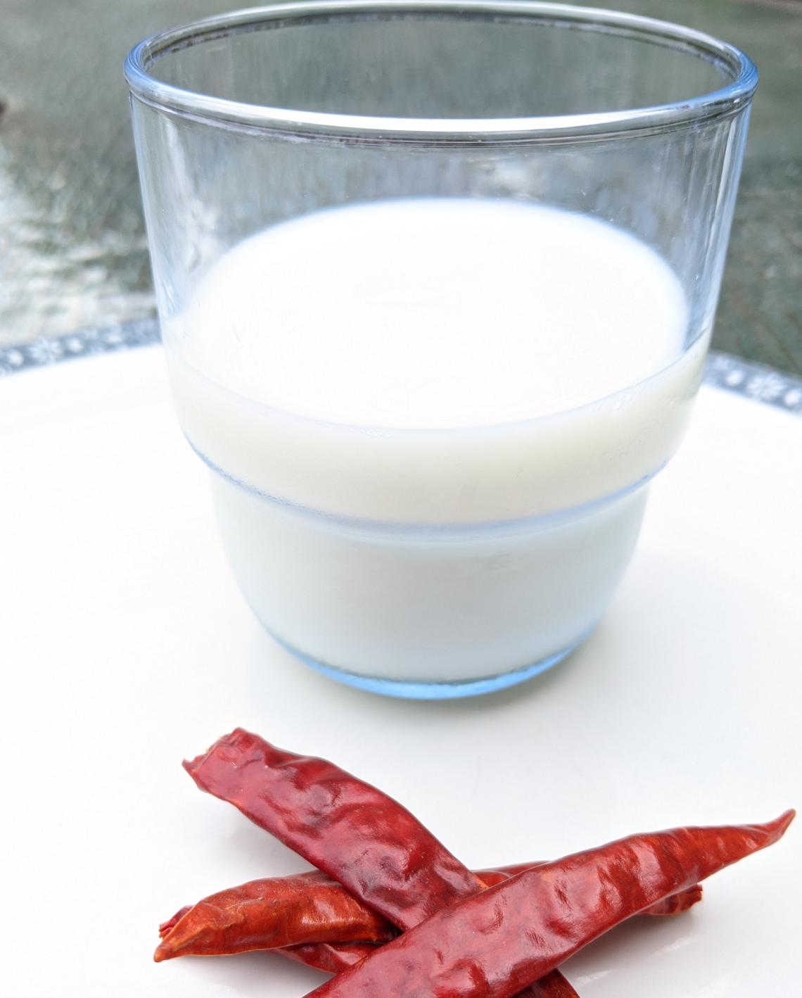 clear glass cup half full of milk & two chili peppers next to it
