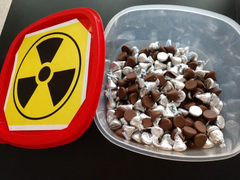 wrapped and unwrapped chocolate kiss candies in a container with radioactive symbol on lid